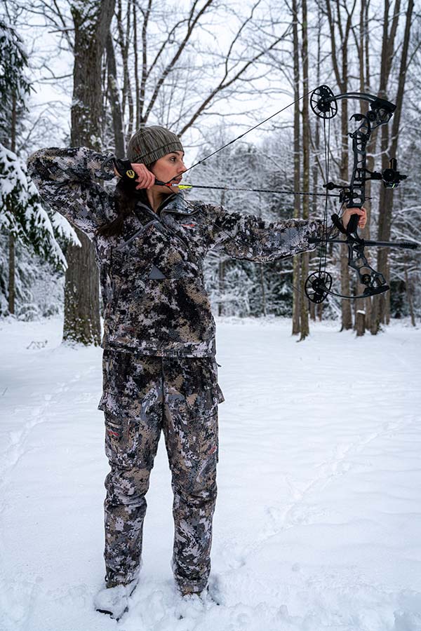 allie atanding in the snow drawing a bow back