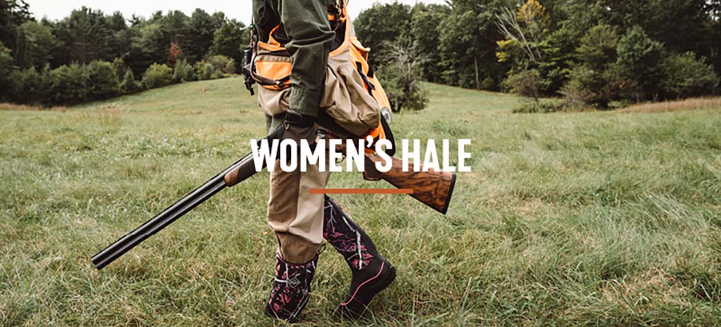 'Women's Hale' Hunter walking through a green field carrying her shotgun and wearing her Hale boots in Muddy Girl Camo
