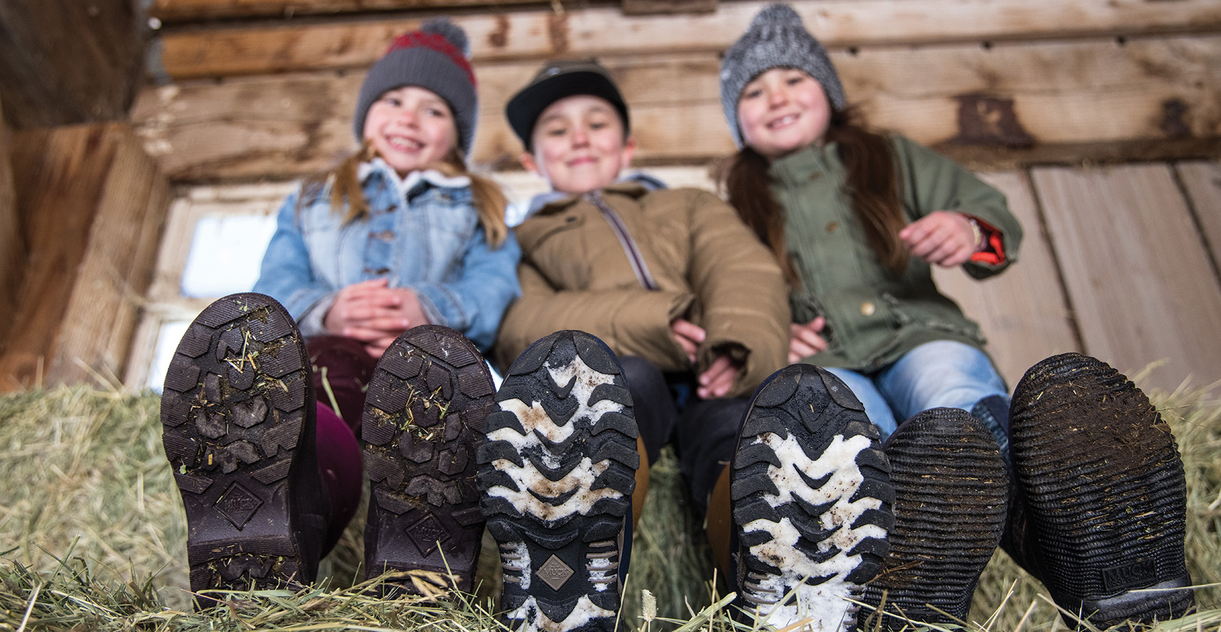 Children with Muck boots on sitting on hay bale