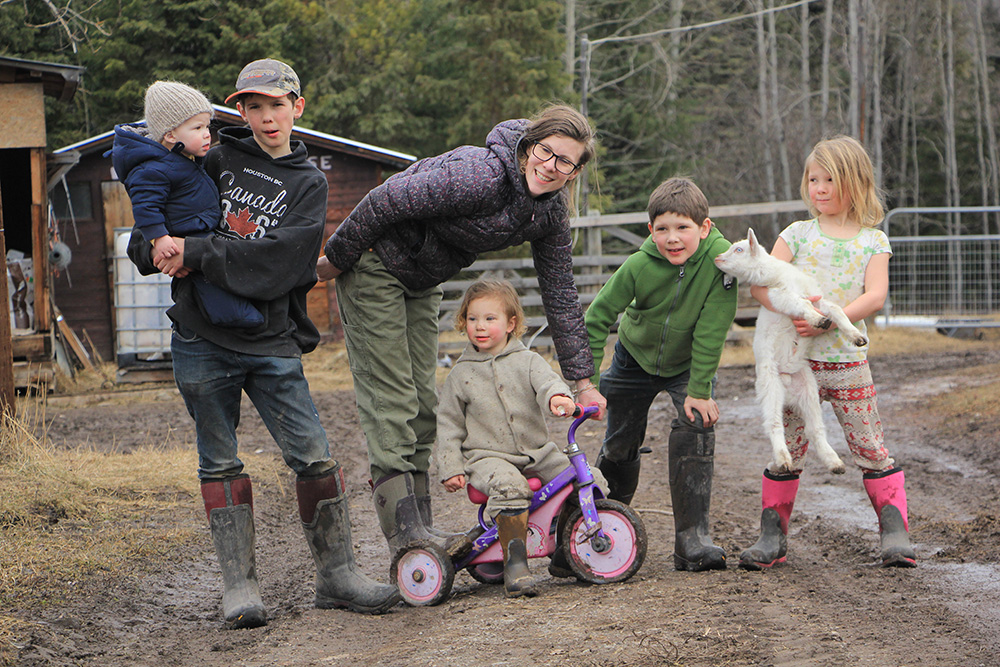 Kate and family on a farm path, wearing various Muck Boots. Her daughter is sitting on a pink and purple tricycle.