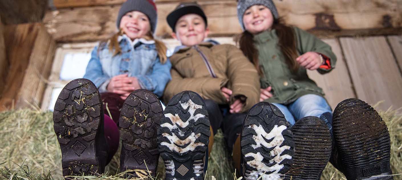 Children sitting in a barn showing their Muck boots