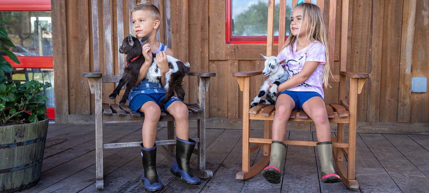 Children sitting on a porch wearing Muck Kid's Forager boots.