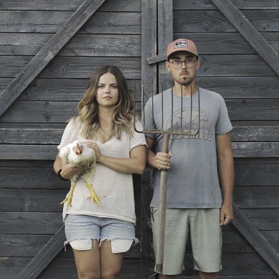 Abbagail standing with her husband holding a chicken and a pitchfork