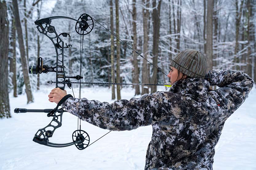 Allie drawing her bow in a snowy forest