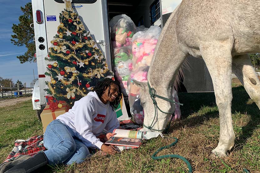 Caitlin Gooch laying on the ground next to a horse reading, and surrounded by Christmas decorations