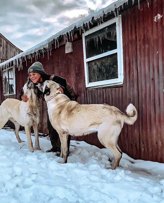 Elizabeth standing outside in front of her barn with her two dogs.