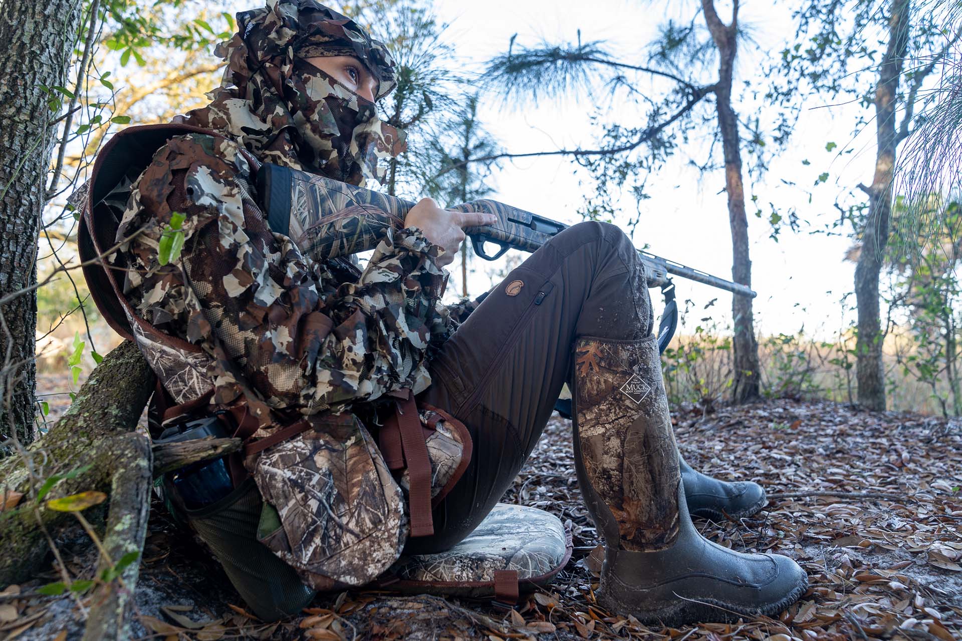 Allie, sitting on the forest floor holding a gun