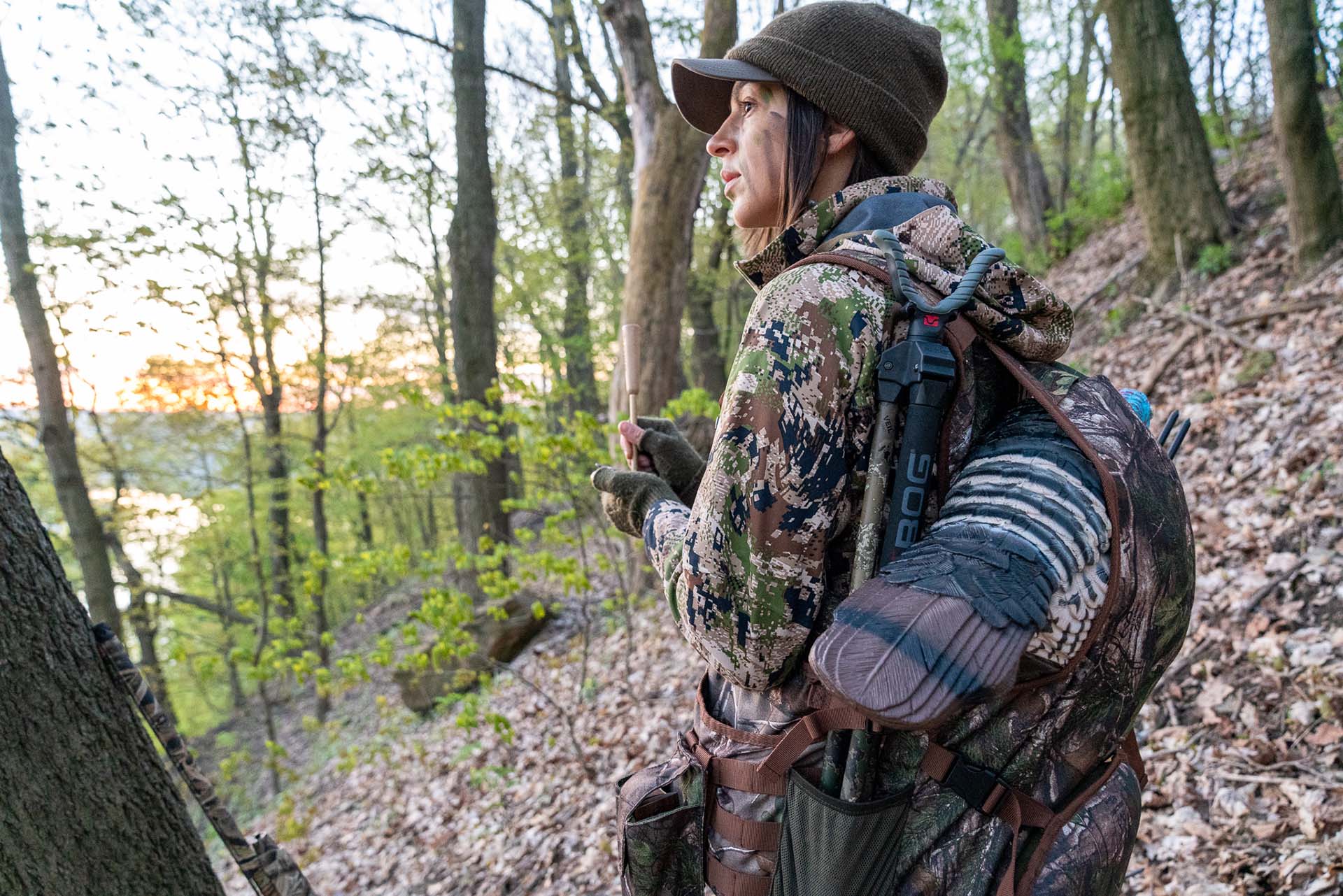 Allie walking through the woods, head to toe in camo gear, carrying turkey on her back