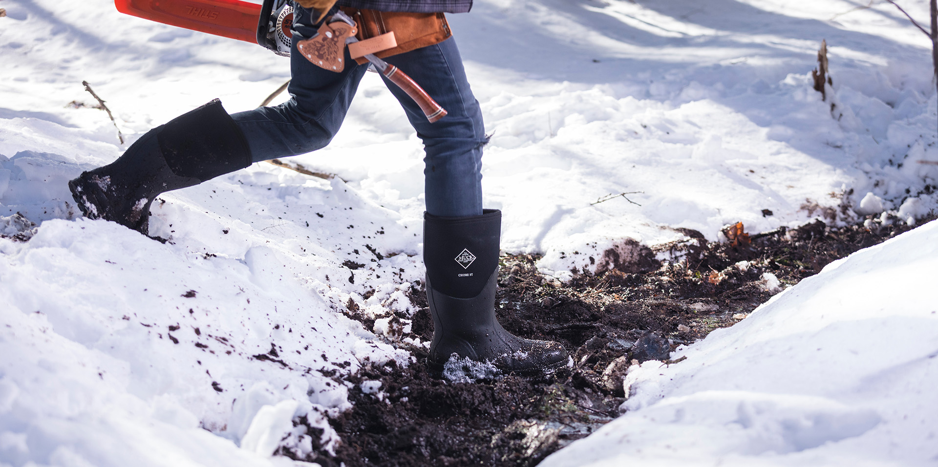 person wearing muck boots in snow while doing chores as a dog stands by them
